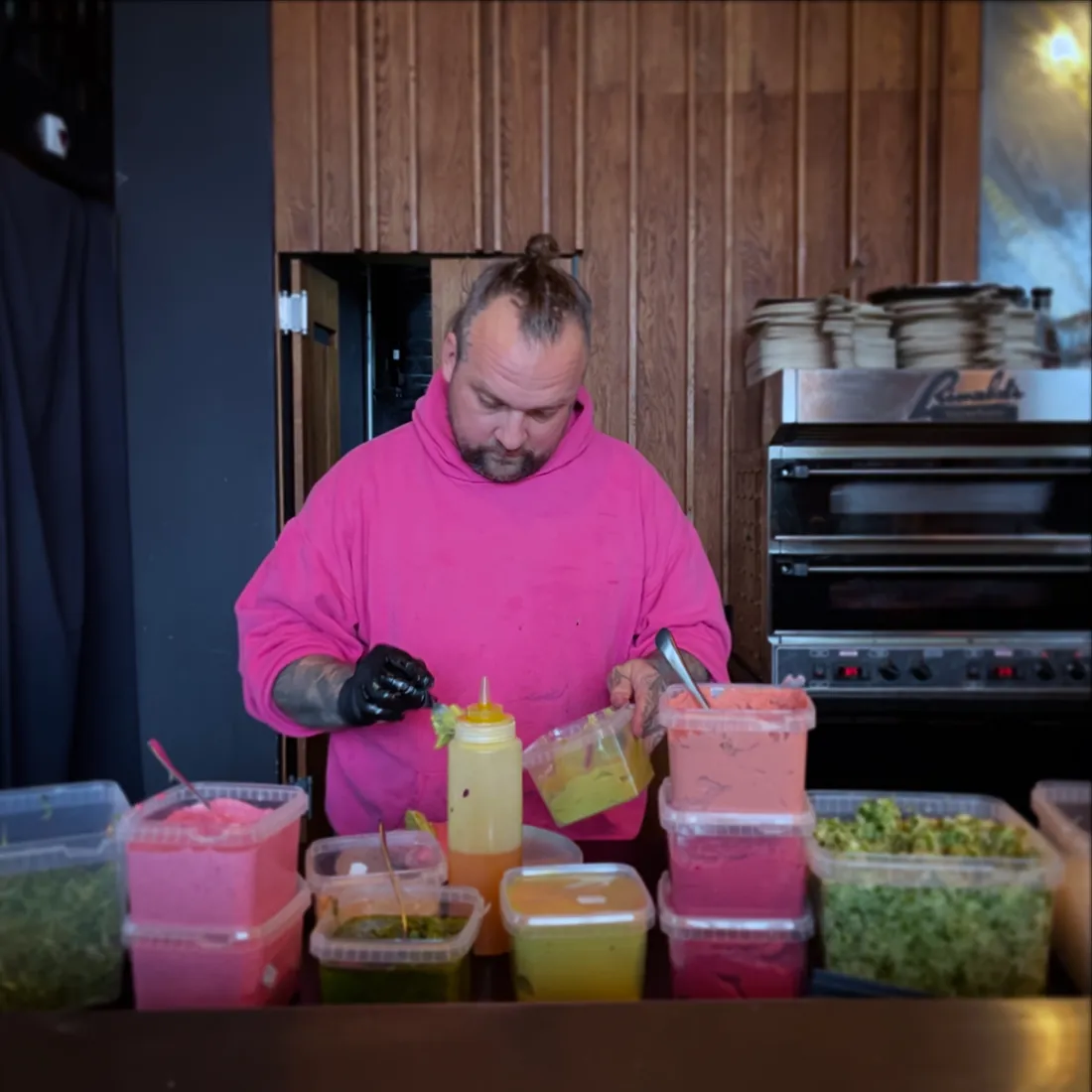 Koch von Colorz Kitchen in pinkem Hoodie beim Anrichten bunter Saucen